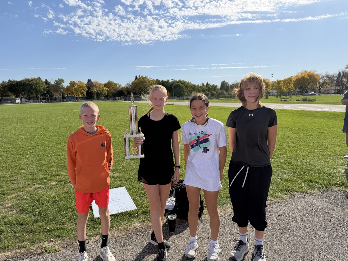 Four Moorhead middle school runners standing on the grass with the tall Amazing Pace trophy