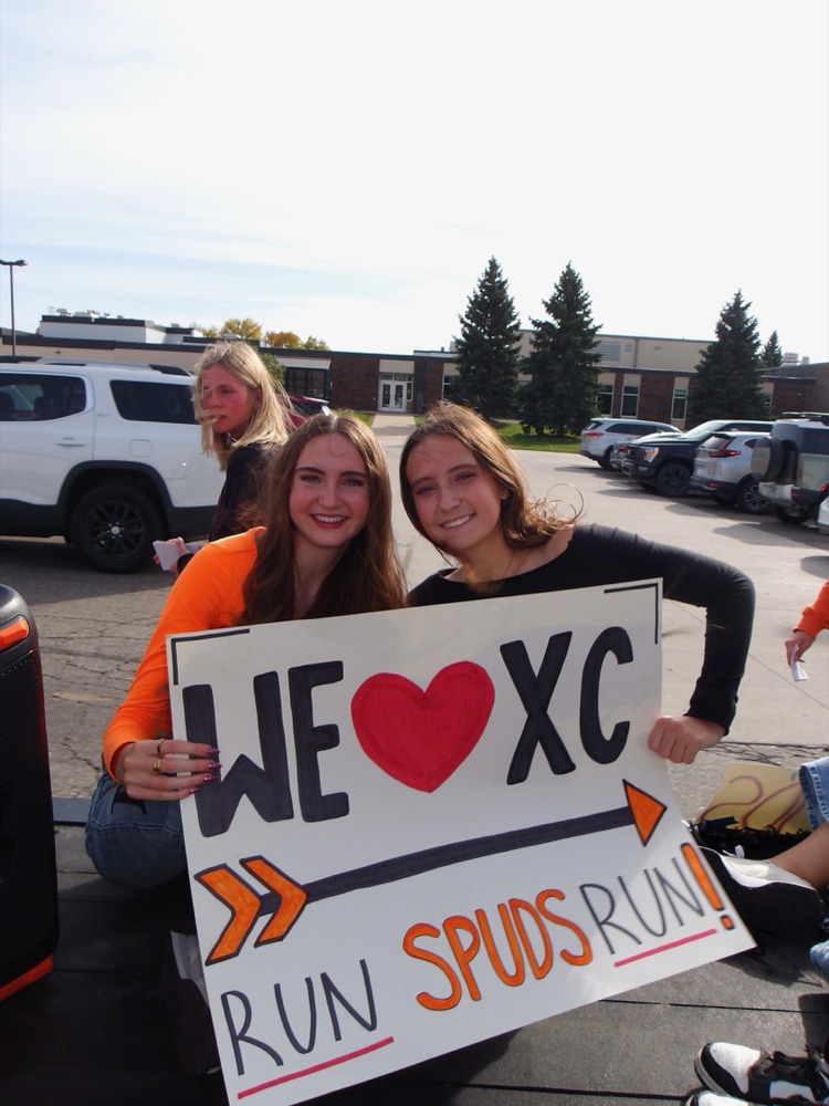 Two Moorhead runners holding a hand lettered We Love XC, Run Spuds Run sign